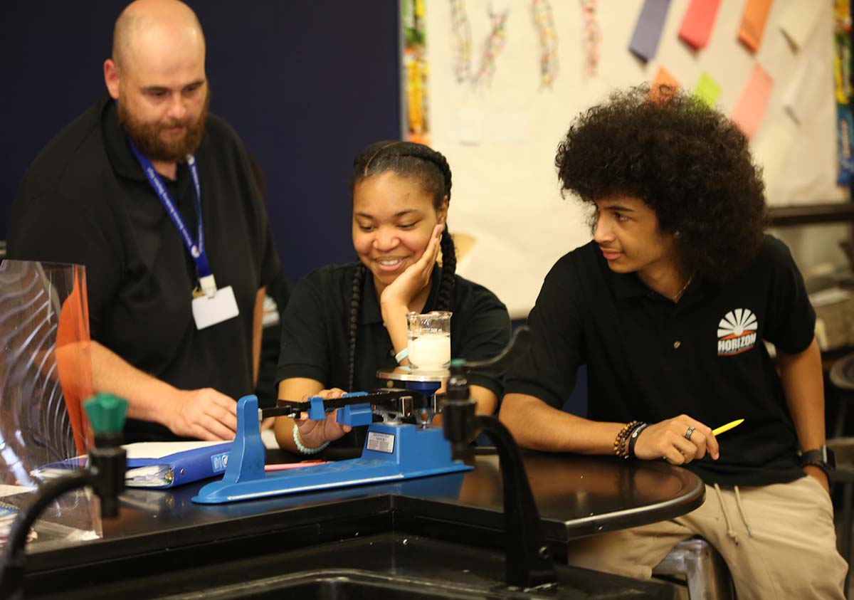 HSA Teacher smiles while kneeling beside a young student in a classroom setting.